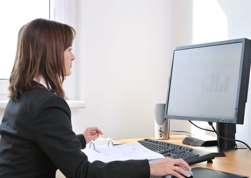 Business person (young woman) works at table with computer - office interior