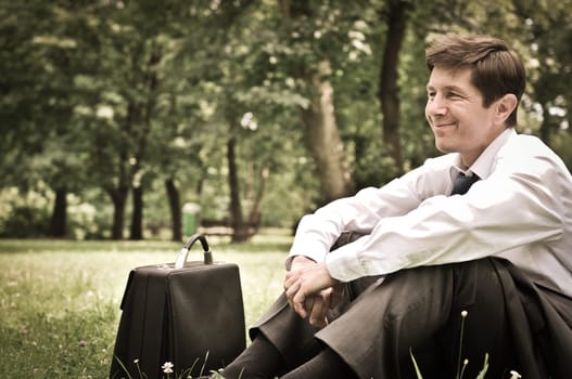 Senior people series - mature business man siting on grass and relaxing in park
