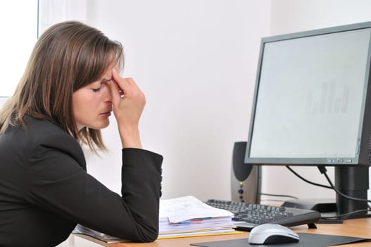 Young business woman with headache and tired closed eyes sitting at computer in workplace