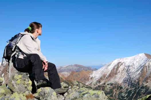 Hiker relaxing on rocky hill with clear blue sky