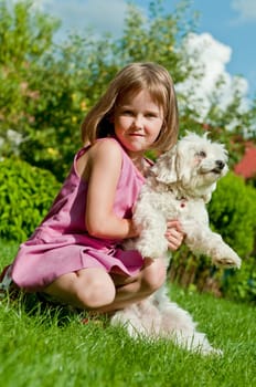 Small cute girl playing with her dog in garden behind family house