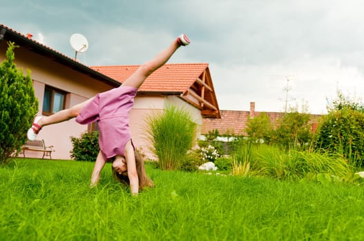 Small girl making cartwheel on garden with family house in background