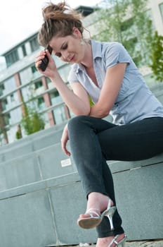 Young worried woman with unhappy expression holding mobile phone - outdoors in urban setting