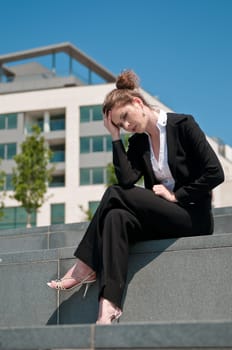 Young worried business woman siting outdoors - head in hand