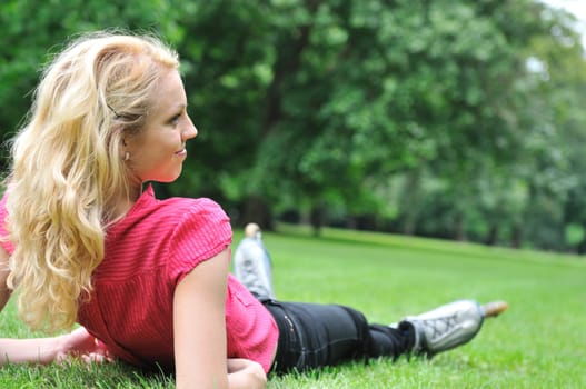 Young smiling woman relaxing in green grass after roller skating - rear view