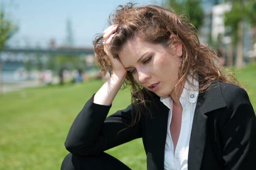 Young worried business woman siting outdoors in grass - head in hand