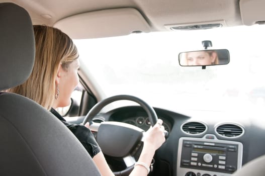 Young cheerful woman driving car - rear view, reflexion of eyes in mirror