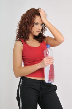 Beautiful tired fitness woman holding forehead with hand with big bottle of water