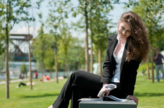 Young business woman sitting outdoors and reading magazine