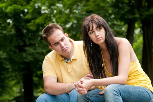 Young couple sitting outdoors on bench having relationship problems