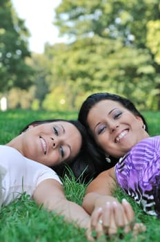 Togetherness - two smiling friends lying in grass outdoors and holding hands