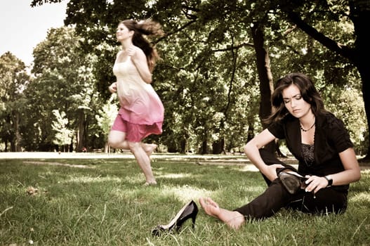 One woman running barefoot in park and second is taking her shoes off