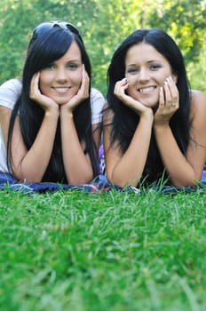 Two smiling friends lying together in grass outdoors with copy space