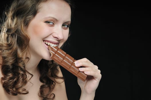 Young beautiful smiling woman eating milk chocolate isolated on black background