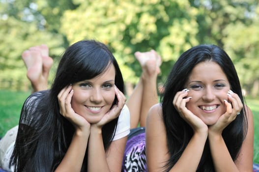 Frendship - portrait of two smiling sisters lying together in grass outdoors with barefeet up
