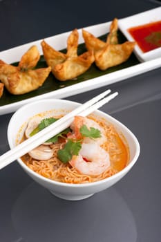 Shrimp and Thai noodle soup bowl with chopsticks along with fried wonton or rangoon type appetizers.