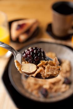 Close up of a spoon full of breakfast cereal flakes with almonds and blackberries.  Shallow depth of field.