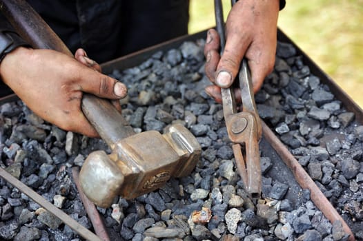 Detail of dirty hands holding hammer and pliers - blacksmith