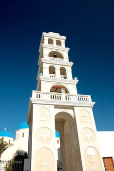 The Bell Tower of the Church in Perissa Santorini Greece under a blue summer sky with the blue domes of the Church in the background