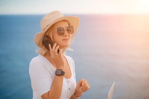 Freelance women sea. She is working on the computer, talking on the phone in the open air with a beautiful view of the sea. The concept of remote work