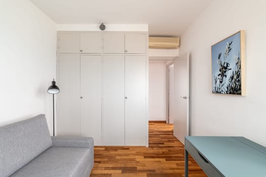 Restored room with white wardrobe grey sofa and table in apartment. Minimalist design of home interior with furnishing. Stylish flat for rent