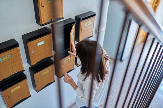 Woman checking mailboxes inside an apartment building. Postal correspondence concept