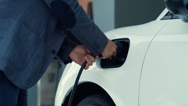 Progressive man attaches an emission-free power connector to the battery of electric vehicle at his home. Electric vehicle charging via cable from charging station to EV car battery