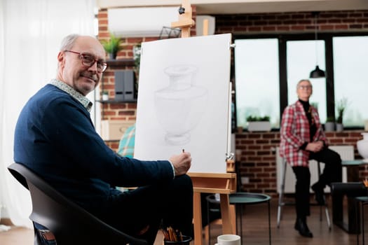 Creative hobbies for adults. Smiling mature man sitting at art studio space, developing creativity in retirement, learning to draw after 50 years. People expressing themselves through drawing