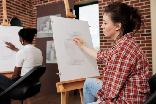 Young woman listening teacher during art workshop learning to draw at beginners group drawing class, creating masterpiece of her own. Stress-relieving creative hobbies for adults