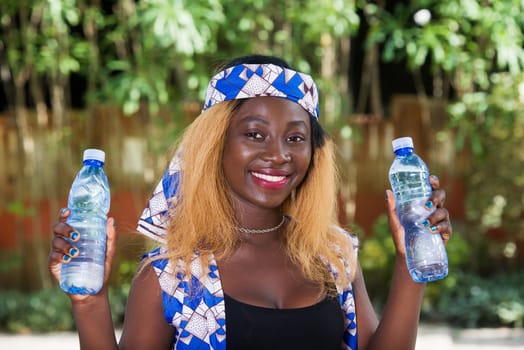 young woman standing outdoors with bottles of water smiling at the camera.