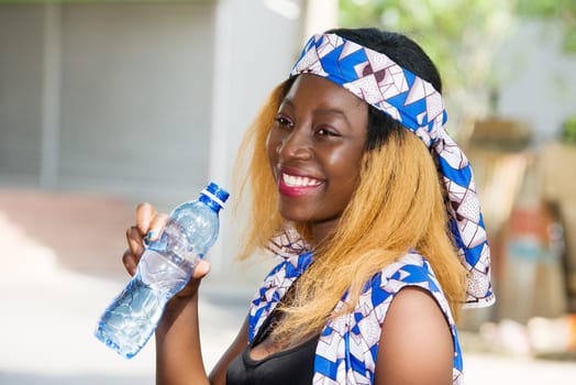 young woman standing outdoors with a bottle of water smiling looking at the camera.