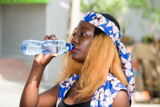 young woman standing outdoors drinking water in a bottle.