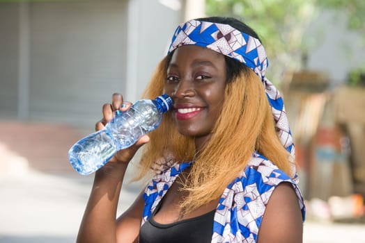young woman standing outdoors with a bottle of water smiling looking at the camera.