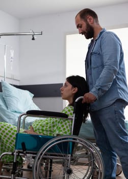 Pregnant woman sitting in wheelchair while future father taking her to maternity room preparing for child delivery in hospital ward. Young couple getting ready for childbirth, discussing parenthood