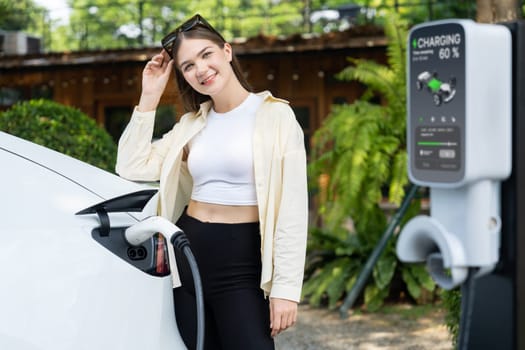 Young woman and sustainable urban commute with EV electric car recharging at outdoor cafe in springtime garden, green city sustainability and environmental friendly EV car. Expedient