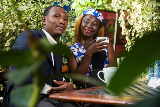 young couple sitting in a park drinking tea while smiling.