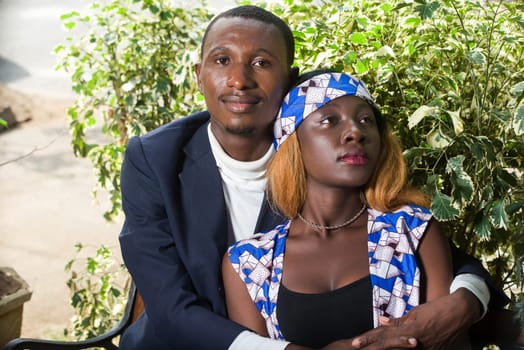 young couple sitting in an embracing park watching the camera smiling.