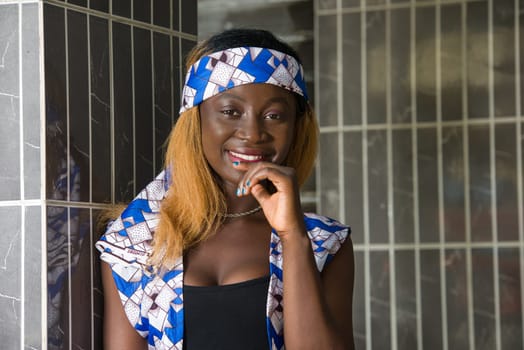 young woman standing near a wall looking at the camera smiling.