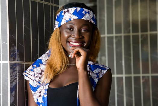 young woman standing near a wall looking at the camera smiling.
