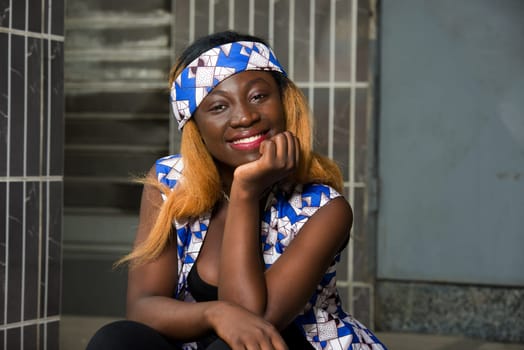 Young girl wearing crown a scarf on her head with hand on chin thinking about the question smiling, woman sitting outside with pensive expression