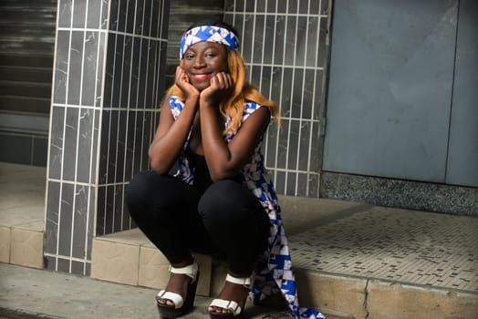 Young girl wearing crown a scarf on her head with hand on chin thinking about the question smiling, woman sitting outside with pensive expression