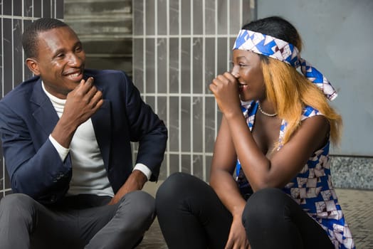 happy couple talking sitting on stairs while laughing and gesturing and looking at each other outdoors.