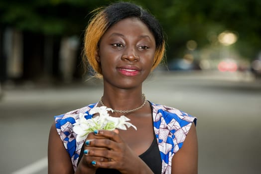 young woman standing outdoors looking at camera smiling with bouquet of flowers in hand.