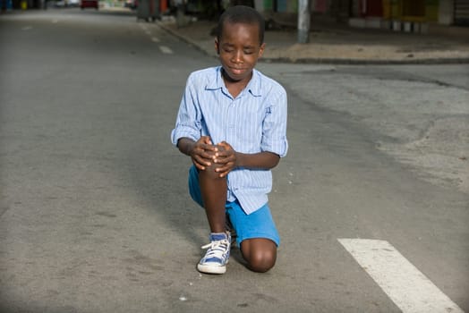 little boy fallen alone on the road crying while holding his injured leg