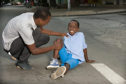 Father comforting his son crying, child fallen on the road having a knee injury