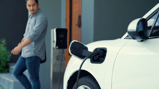 A man unplugs the electric vehicle's charger at his residence. Concept of the use of electric vehicles in a progressive lifestyle contributes to a clean and healthy environment.