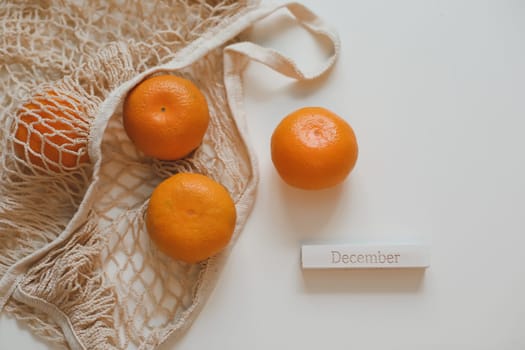 Christmas or New Year composition with fresh tangerines in shopping bag and word December.
