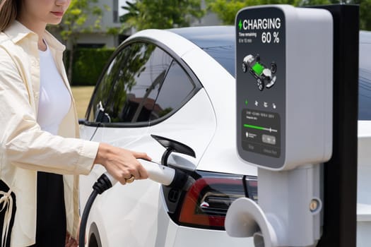 Young woman put EV charger to recharge electric car's battery from charging station. Alternative energy and rechargeable EV car for sustainable environmental friendly travel concept. Expedient