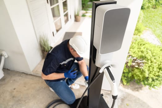 Qualified technician install home EV charging station, providing maintenance service for electric vehicle's battery charging platform at home. EV car technology for residential utilization. Synchronos