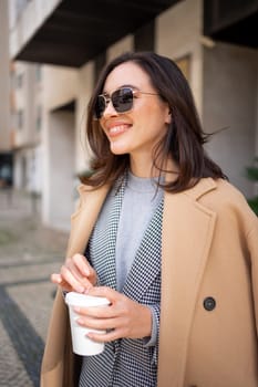 Streetstyle, street fashion concept: woman wearing trendy outfit walking in city. Cream trench coat, sunglasses. Side view Looking away, vertical photo